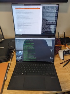 Photograph of a laptop with two displays; the second display is underneath where the keyboard normally sits.  In this photograph the keyboard is detached and sitting on a desk in front of the two fully visible displays.